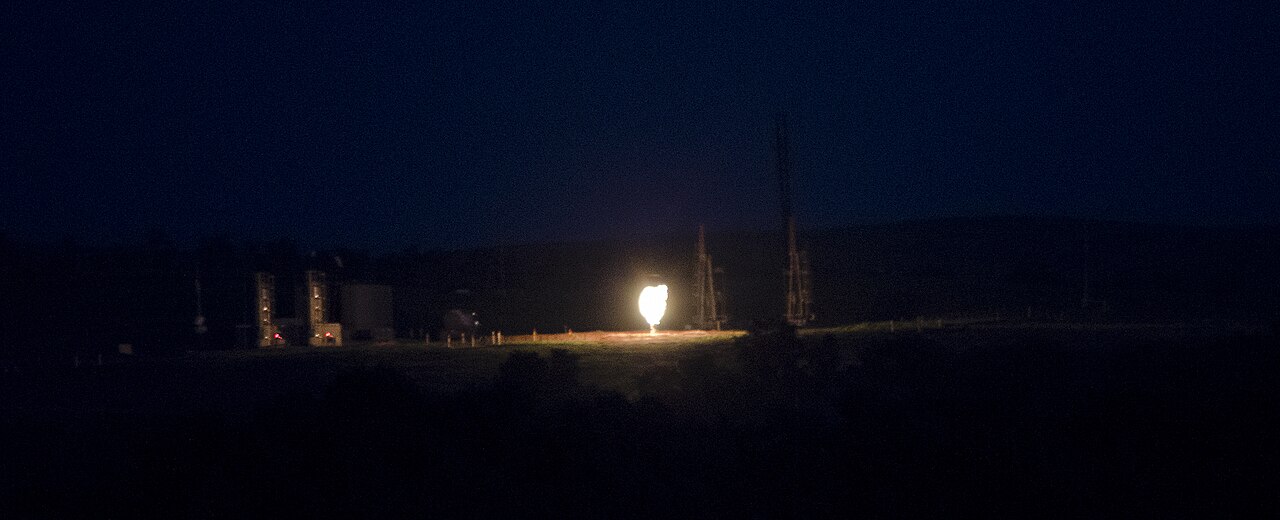 Natural gas flare burning at night in North Dakota, symbol of the physical supply shocks behind energy tail risk